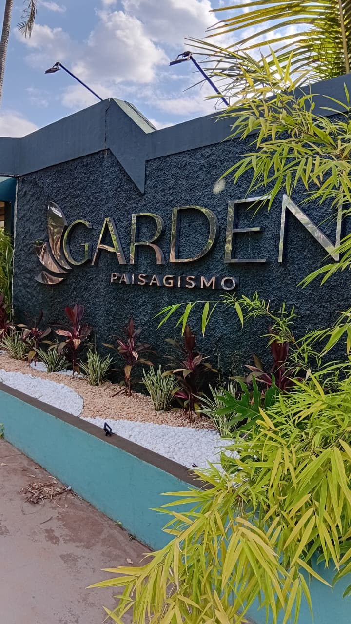 Fachada da Garden Paisagismo, com o letreiro na parede escura e canteiro de plantas